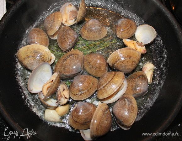 Добавляем клемы и обжариваем их одну минуту. Вливаем вино, солим, накрываем крышкой и готовим 3-5 минут.