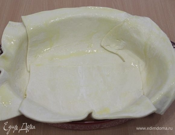 Слоеное тесто выложить в форму, так чтобы края свисали, смазать сливочным маслом.