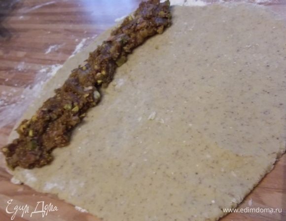 На посыпанной мукой поверхности (мне пришлось добавить приблизительно 2 ст. л. муки, домешивала прямо на поверхности) разделить тесто на 2 части, раскатать в прямоугольник, выложить половину начинки и закрутить в плотный рулет. Залепить края. 