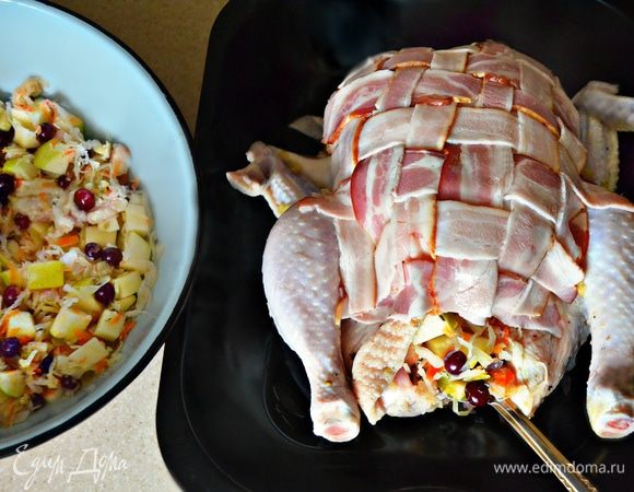 Окутать курочку с двух сторон плетенкой из бекона и закрепить с помощью зубочисток. С квашенной капусты слить лишнюю жидкость, добавить клюкву и нарезанное яблоко, перемешать. Наполнить курицу начинкой и закрепить зубочистками. 