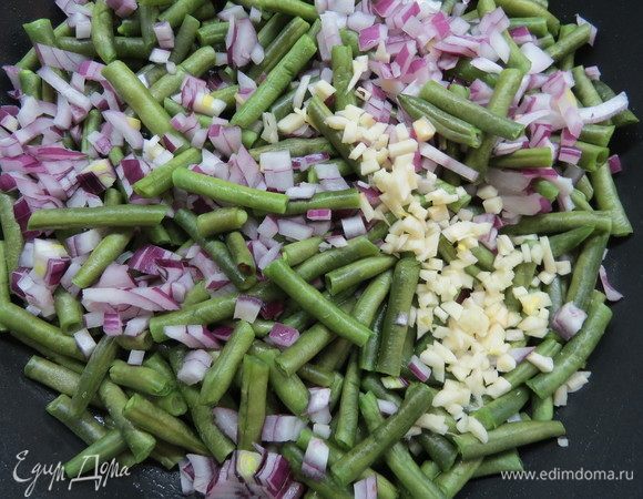 Закладываем в сковороду зеленую фасоль и обжариваем ее на сливочном масле 10–15 минут. Тем временем мелко нарезаем одну луковицу и чеснок. Добавляем их в сковороду и обжариваем 5 минут, помешивая.