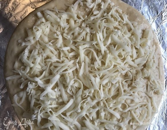 Переверните лепешку и немного раскатайте. Выложите хачапури на бумагу для выпечки, смажьте взбитым желтком и посыпьте сыром.