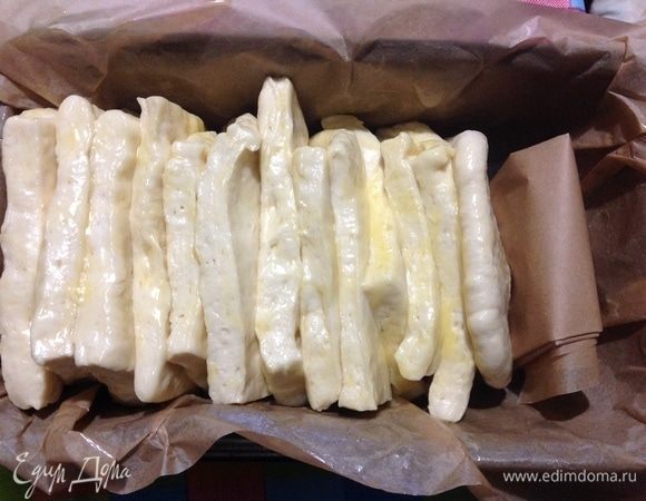 Смазанные квадраты я складывала в стопку на тарелке. Духовку уже включаем на нагрев 190°С.
Форму для выпечки я застелила пергаментным листом, чтобы легче было вынимать нестандартный хлебушек.
Складываем в застеленную форму стопки квадратов теста, и у нас остается пустое место в длину до конца формы, это очень правильно, потому что хлеб еще будет расстаиваться и увеличится в длину тоже. В это пустое место пока ставим распорку из пергамента для того, чтобы стопка квадратов не завалилась на бок.