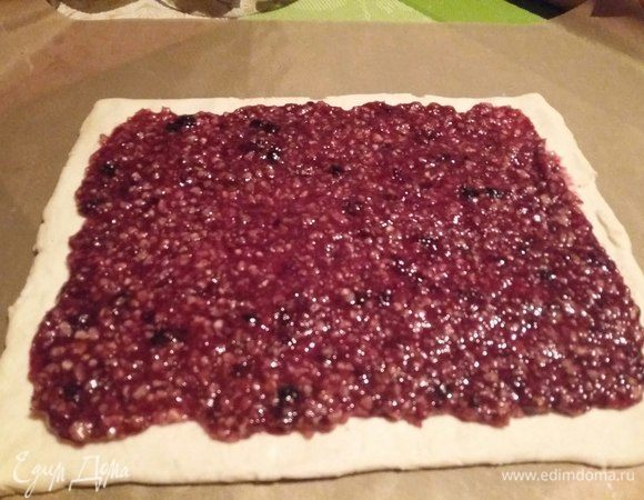 Пласт теста немного раскатать, выложить на противень, застеленный либо силиконовым ковриком, либо пергаментом. На тесто распределить ровным слоем начинку, оставив края свободными. Края смочить водой при помощи силиконовой кисточки. 