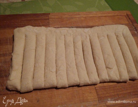 Теперь взять второй пласт теста, чуть припылить мукой одну сторону, сложить пополам и ножом сделать разрезы от линии сгиба, не разрезая примерно 2 см от края. 