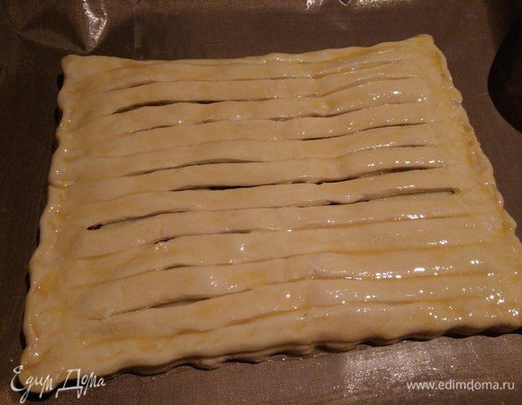 Накрыть начинку раскрытым пластом теста с разрезами. Смазать верх пирога яичным желтком. Выпекать в духовке при 200°С, 20-25 минут до золотистого цвета.