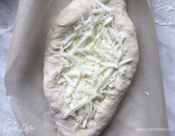 Растяните порцию теста в прямоугольник длиной примерно 25 см и шириной 8–10 см. Отступив от краев по 1,5 см, выложите сыр. Накиньте длинные стороны теста на начинку. Узкие края соедините и перекрутите. Прижмите лодочку ладонью, чтобы она стала более плоской.