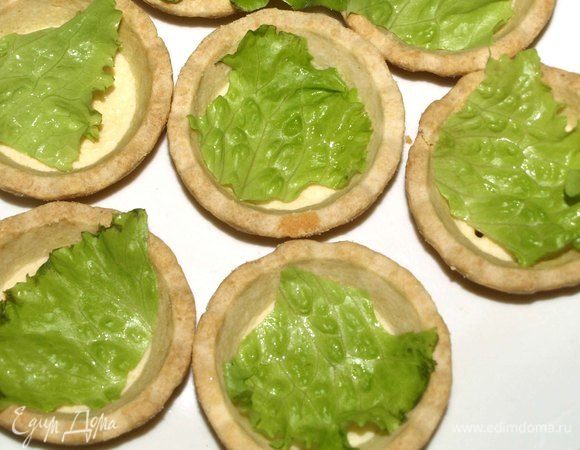 Тарталетки берем готовые или, при желании, делаем сами. У меня покупные. Чтобы тарталетки не размокли от начинки раньше времени, выкладываем внутрь тарталетки небольшой кусочек зеленого салата (все при желании и наличии листьев салата). 