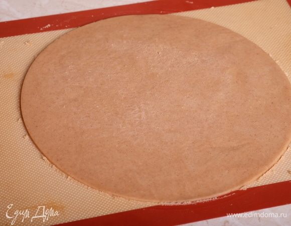 Выпечем коржи из песочного теста. Охлажденное тесто разделить пополам. Раскатать первую часть теста на силиконовом коврике до толщины 3–5 мм. Раскатывать нужно через лист пергамента — так тесто не будет приставать к скалке. Вырезать вырубкой, равной диаметру торта (26 см), круг. Охладить его прямо на коврике в холодильнике минимум 2 часа. Остатки теста сохранить.