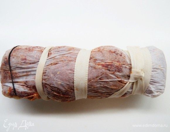 Заворачиваем мясо в пергамент, чтобы придать куску удобную для нарезки форму, можно обмотать мясо кулинарной нитью (у меня нить закончилась, поэтому использовала широкую резинку).
Положить мясо в холодильник на верхнюю полку двери и оставить вялиться на 25–30 суток. В первые дни проверять состояние пергамента, если намок, заменить на сухой. Дней через 5 пергамент намокать перестанет.