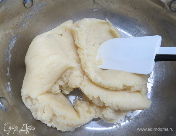 Как только масса закипела, выключить огонь и всыпать всю муку разом. Быстро размешать деревянной лопаткой до однородности, так чтобы не осталось комков. Вернуть тесто на плиту и на среднем огне нагревать, непрерывно мешая, пока тесто не соберется в гладкий шар, а на дне кастрюли не появится бархатный мучной налет. Он ни в коем случае не должен быть горелым, только белым, будто дно посыпали мукой. Это помогает выпарить из теста лишнюю воду, чтобы водяной пар в процессе выпечки не разорвал наши пирожные. Снимаем с огня и даем пару минут остыть. Потрогайте тесто пальцем, оно не должно быть очень горячим, иначе яйца сварятся. 