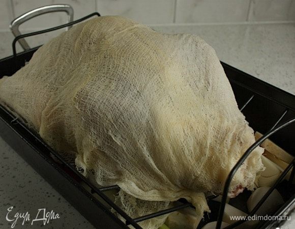 Вынуть замоченную марлю, слегка отжать и разложить на индейке как есть — в 4 слоя, прикрывая ноги. 
Поместить индейку в духовку ногами к задней стенке и готовить 30 минут (я добавила 0,5 ст. горячей воды к овощам, т.к. боялась, что они сгорят). Затем, используя кулинарную большую кисть, смочить марлю и неприкрытые части винно-масляной смесью (марля станет коричневой, не пугайтесь!).
Убавить температуру до 180°С и готовить 1,5 часа, смачивая марлю каждые 30 минут. Из индейки будет выделяться мясной сок и жир, поэтому нужно следить за жидкостью в жаровне. Ее не должно быть много, чтобы птица не плавала в ней, но и не допускать, чтобы жидкость вообще отсутствовала. Можно доливать воды по чуть-чуть. 
После 2 часов запекания (от начала) снять и выбросить марлю. Повернуть жаровню на 180°С. Полить индейку соками из жаровни или винно-масляной смесью. Кожа становится золотисто-коричневой и хрупкой, поэтому нужно тщательно смачивать ее, особенно грудку. Если слишком поджариваются какие то части, накрыть их фольгой.
Через 30 минут проколоть вилкой толстую часть бедра. Грудку не проверять. Вытекающий сок должен быть прозрачным и без крови. Если нет, то готовить еще 30 минут.
Готовую индейку переложить на сервировочное блюдо, накрыть фольгой не слишком плотно и дать отдохнуть 20-30 минут.