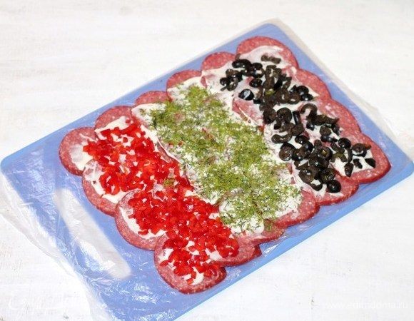 Выкладываем нарезанные продукты на сыр и сворачиваем в рулет. Пленку освобождаем и при помощи ее, заворачиваем скрученный рулет, как конфету.