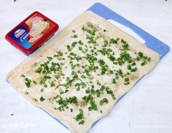 Плавленный сыр Hochland смешиваем с 2 ст. л. куриного белка. Можно добавить по вкусу соль и молотый перец. Смазываем пласт теста сырной смесью. Мелко нарезаем перья зеленого лука и выкладываем на сыр. Куриный белок добавляем для того, чтобы при выпечке, сыр не растекался.
