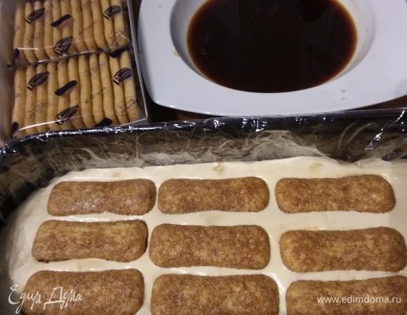 Заранее сварить крепкий кофе, смешать с миндальным ликером. Мысленно разделить крем на три части. Большую продолговатую форму выложить пищевой пленкой с запасом. Выложить третью часть крема, окунуть савоярди в кофе и выложить слой бисквита. Я чего-то «поскромничала» и выложила палочки савоярди слишком редко.