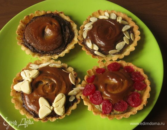 Украшаем произвольно — сахар, лепестки миндаля (у меня самодельные, еще 15 г миндаля на украшение), вишенки коктейльные по две штучки и еще пару кружков на одну корзинку, украшение из белого шоколада (растапливаем на водяной бане и наливаем в формы). Курд пропитывает основу тарталетки, через два дня этот слой практически не виден в разрезе (пару корзинок оставляла для новогоднего подарка), но дает тонкий вкус лимона шоколаду. И еще, при запекании основы положила в пару корзинок зернышки на удачу в новом году. Приятного аппетита!