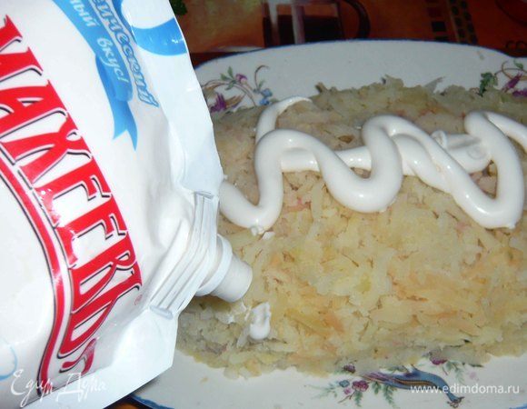 На терке трем картофель и выкладываем на хамсу с луком. Сверху добавляем майонез и равномерно распределяем по слою картофеля.