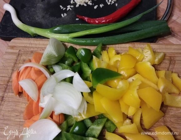 Тем временем подготовить остальные ингредиенты. Перцы и морковь очистить и нарезать. Лук и чеснок очистить. Лук нарезать перьями, а чеснок мелко порубить или растереть с солью. 