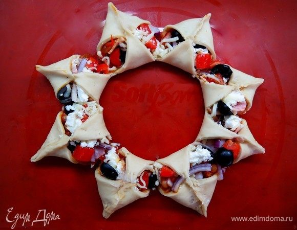 Отрезки центральной части лепешки кладем на начинку. Концы каждого треугольника соединяем, залепляем так, чтобы получился закрытый треугольник. Таким образом наша пицца приобретает форму венка. Оставляем венок на 10-15 минут, затем смазываем взбитым желтком. Выпекаем в предварительно разогретой духовке, при температуре 180°С 20 минут. 