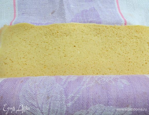 Готовый, еще горячий бисквит переворачиваем на чистое кухонное полотенце и снимаем пергамент. Переворачиваем бисквит и сворачиваем вместе с полотенцем в рулет. Охлаждаем до комнатной температуры.