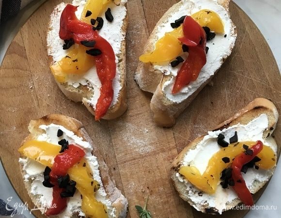 Выложите на хлеб творожный сыр, перец, маслины измельченные и украсьте зеленью.