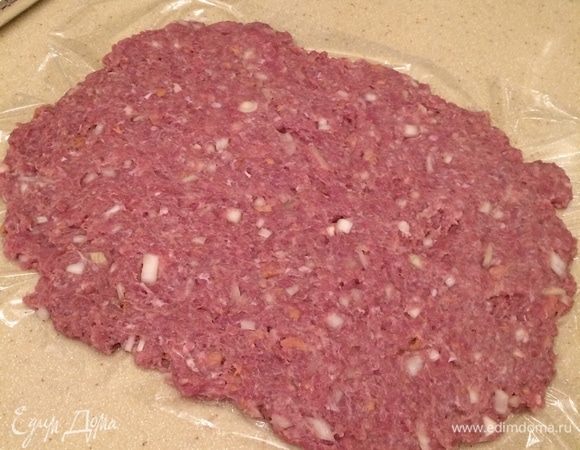 Из данного количества фарша получается 2 рулета. Фарш разделить на 2 части. Духовку разогреть до 180°С. На столе расстелить пищевую пленку. Выложить первую часть фарша, утрамбовать смоченными холодной водой руками фарш так, чтобы получился прямоугольник размером примерно 30х25 см и толщиной 1 см.