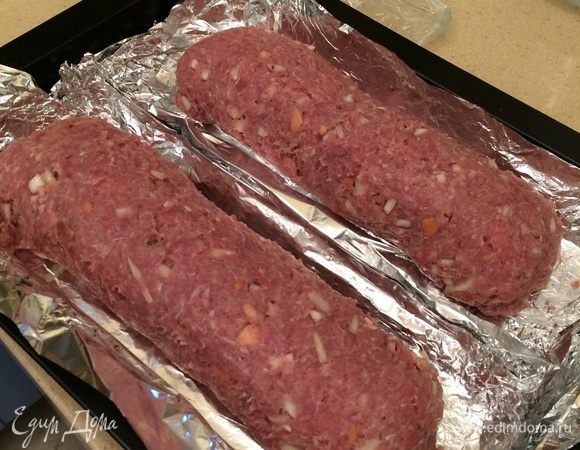 Приподнимая края пленки, свернуть аккуратно рулет, края защипать. Глубокую форму для выпечки (противень) выстелить фольгой, выложить первый рулет. То же самое сделать со второй частью фарша и начинки. Выложить в тот же противень второй рулет.