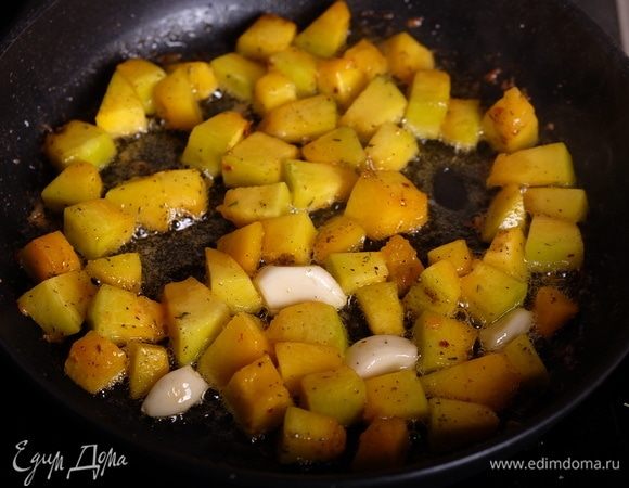 Через 5 минут готовки добавить целые зубчики чеснок и жарить до образования на кубиках тыквы румяной корочки. Если чеснок начнет подгорать — вынуть его.