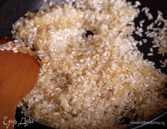 Добавить к луку рис, перемешать, чтобы каждая рисинка была в масле. Рис ни в коем случае предварительно не промывать.