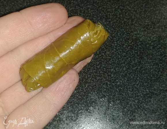 Дальше мы заворачиваем получившуюся смесь из фарша, риса, лука и зелени в промытые виноградные листья. Лист кладем шершавой (матовой) стороной вверх. Кончик листика срезается. Затем мы выкладываем небольшое количество фарша на лист (острой стороной лист лежит от нас). Накрываем фарш стороной листа ближней к нам (той стороной с которой мы срезали кончик). Затем заворачиваем стороны листа на начинку (справа и слева). И закатываем долму в оставшуюся часть листа (просто крутим по направлению от нас). В итоге у нас получается небольшая трубочка.