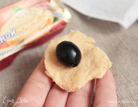 Теперь, отщипывая тесто небольшими кусочками, чтобы можно было завернуть в него оливку, сформовать шарики. Из кусочка сделать лепешечку, в центр кладем оливку черную или зеленую, защипнуть тесто в узелок и покатать между ладоней, чтобы получился ровный шарик. Оливки должны быть хорошо обсушены.
