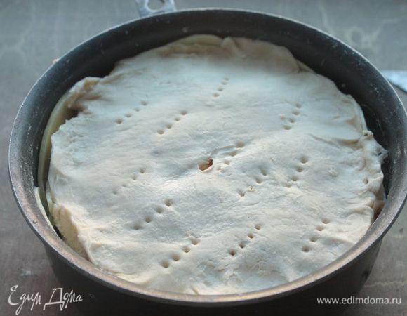 Поверх него укладываем слоеное тесто, вырезанное по форме основания пирога, и протыкаем его в нескольких местах.