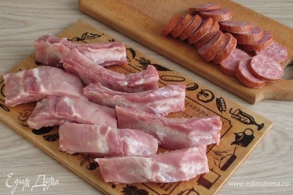 Свиные ребра нужно нарезать на кусочки по 1–2 косточки, а колбасу — на кружочки толщиной около 0,5 см.