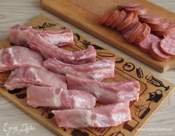 Свиные ребра нужно нарезать на кусочки по 1–2 косточки, а колбасу — на кружочки толщиной около 0,5 см.