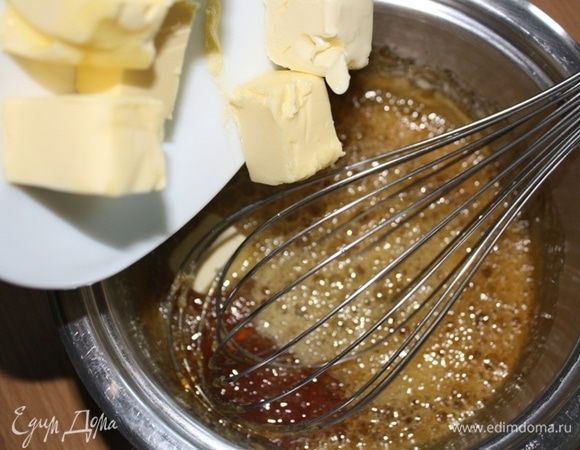 Далее добавляем холодное сливочное масло кусочками и тщательно перемешиваем до однородности. Затем переливаем в миску (если остались небольшие кусочки карамели, используем сито) и даем остыть до 60°С.