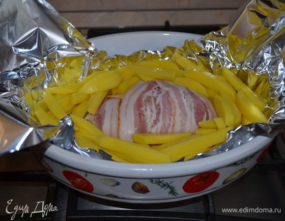 В форму для запекания положить фольгу. Выложить на нее куриное филе, завернутое в бекон. Вокруг выложить картофель, оставшееся масло из тарелки вылить на картофель. Прикрыть сверху фольгой, перед тем, как отправить в духовку.