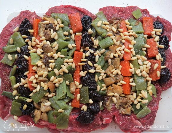 Мясо посолить и поперчить, выложить начинку, чередуя полосами фасоль, чернослив, морковь, грибы по всей ширине рулета. Сверху посыпать кедровыми орешками.