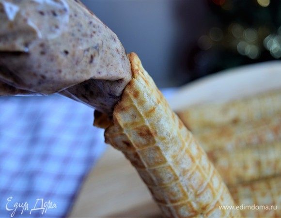 Переложите начинку из орехов и фиников в кондитерский пакет или пакет целлофановый, отрезав маленький уголочек. Выдавите начинку в каждую трубочку с двух сторон, насколько получится. Трубочки будут полыми посередине. (По желанию, можно сделать начинку до приготовления вафель и уже свернуть готовые вафли с начинкой. А затем немного добавить начинку по бокам в уже свернутые вафли). Насыпьте на плоскую поверхность кокосовую стружку и обмакните начинку по бокам вафель.