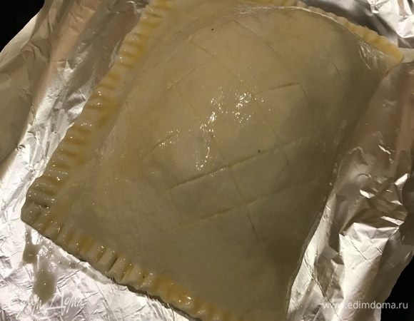 Переложите мясо на противень, выстеленный бумагой для выпечки, смажьте тесто яйцом.