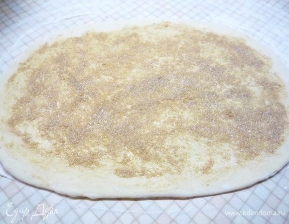 Разделим тесто на две части (будет два венка). Рабочую поверхность присыпаем мукой и раскатываем тесто в прямоугольный пласт (не толще 5 см). Для начинки растираем сливочное масло комнатной температуры, сахар и корицу в пасту. Распределяем по поверхности теста, отступая от краев примерно 1 см.