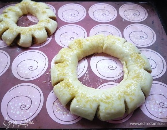 Перекладываем кольца на противень, делаем на каждом кольце снаружи по 12 поперечных надрезов. Накрываем полотенцем и оставляем еще на 20-30 минут подниматься. Яйцо слегка взбиваем и смазываем им кольца, сверху посыпаем тростниковым или жемчужным сахаром. Выпекаем в заранее разогретой духовке при температуре 180°С 20-25 минут.