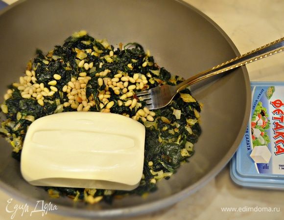 Добавьте к шпинату сыр фетакса Hochland и хорошо разомните его вилкой, затем добавьте обжаренные кедровые орешки и перемешайте.