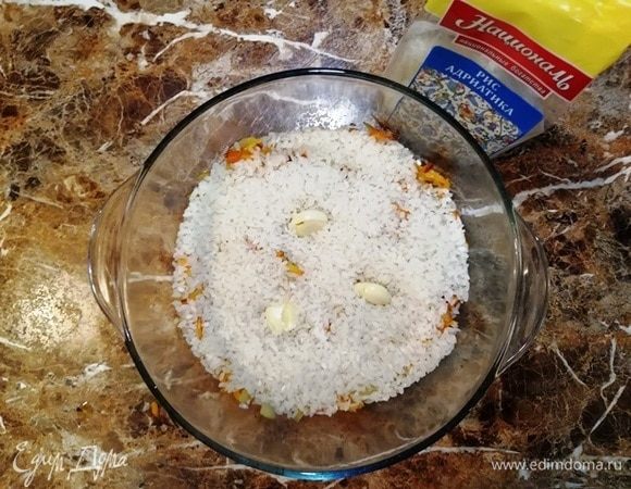 Рис промойте, слегка обсушите и выложите на смесь лука и моркови.
Выложите чеснок.