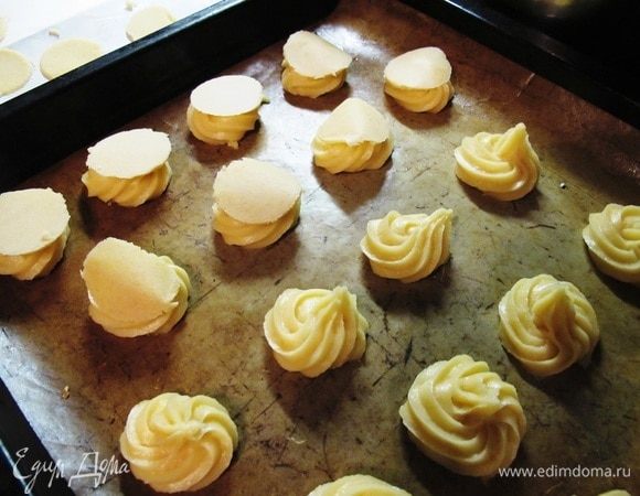 Готовое тесто отсадить на противень, на бумагу для выпечки, кружками диаметром около 5 см на расстоянии друг от друга, так как булочки будут сильно увеличиваться при выпечке.
Достать из морозилки кружки первого теста и положить сверху на каждую булочку.