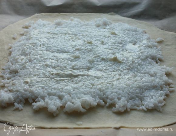 На тесто, отступая от краев примерно по 5 см, выложите рис и смажьте его тонким слоем мягкого сливочного масла.