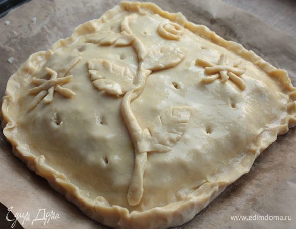 Из обрезков теста, по желанию, сделайте украшения. Также сделайте несколько отверстий в пироге, а в конце смажьте поверхность пирога взбитым яйцом и отправьте его в духовку выпекаться 30–40 минут при 180°С (без конвекции).