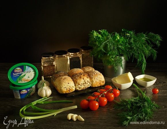 Подготовим необходимые ингредиенты. 
Нам нужны булочки, посыпанные маком, кунжутом, семенами льна и семенами подсолнечника или другие красивые зерновые булочки. Для фарширования 12 булочек небольшого размера нам потребуется 2 ванночки творожного сыра Hochland с зеленью. Также нам необходимы помидоры черри, чеснок, сливочное масло, оливковое масло, укроп или любая зелень, которая вам нравится. Ну, а если у вас на обед будет борщ, тем, кто окажется рядом с вами, просто повезло!