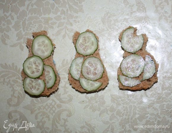 На каждый кусочек выложить тонко нарезанные огурчики. 
