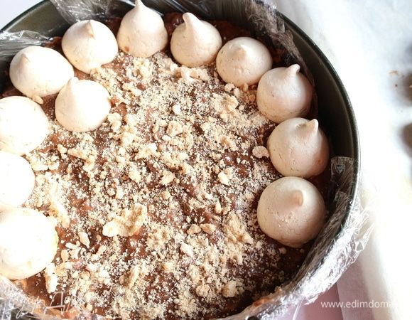 Слегка поджарить орехи на сухой сковороде. Дать остыть. Измельчить в блендере. Приготовить крем. Желток смешать с молоком, сахарным песком и ванильным сахаром.  Поставить на маленький огонь в сотейнике с толстым дном примерно на 4–5 минут, постоянно помешивая. Масло, которое следует достать из холодильника заранее, взбить с какао-порошком, коньяком, добавить полностью остывший крем, перемешать. Затем добавить орехи, перемешать. Дно круглой разъемной формы застелить пленкой, выложить безе по дну формы, затем аккуратно, чтобы не разрушить безе, заполнить кремом. Сверху поместить еще один ряд безе. Четыре-пять штук безе надо оставить при этом на крошку.