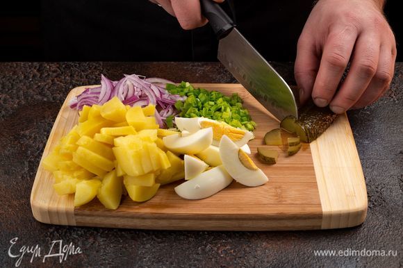 Приступим к приготовлению салата. Вареный картофель очистите и нарежьте ломтиками. Также нарежьте кубиками яйца, маринованные огурцы. Зеленый и репчатый лук мелко нарежьте, с кукурузы слейте жидкость.